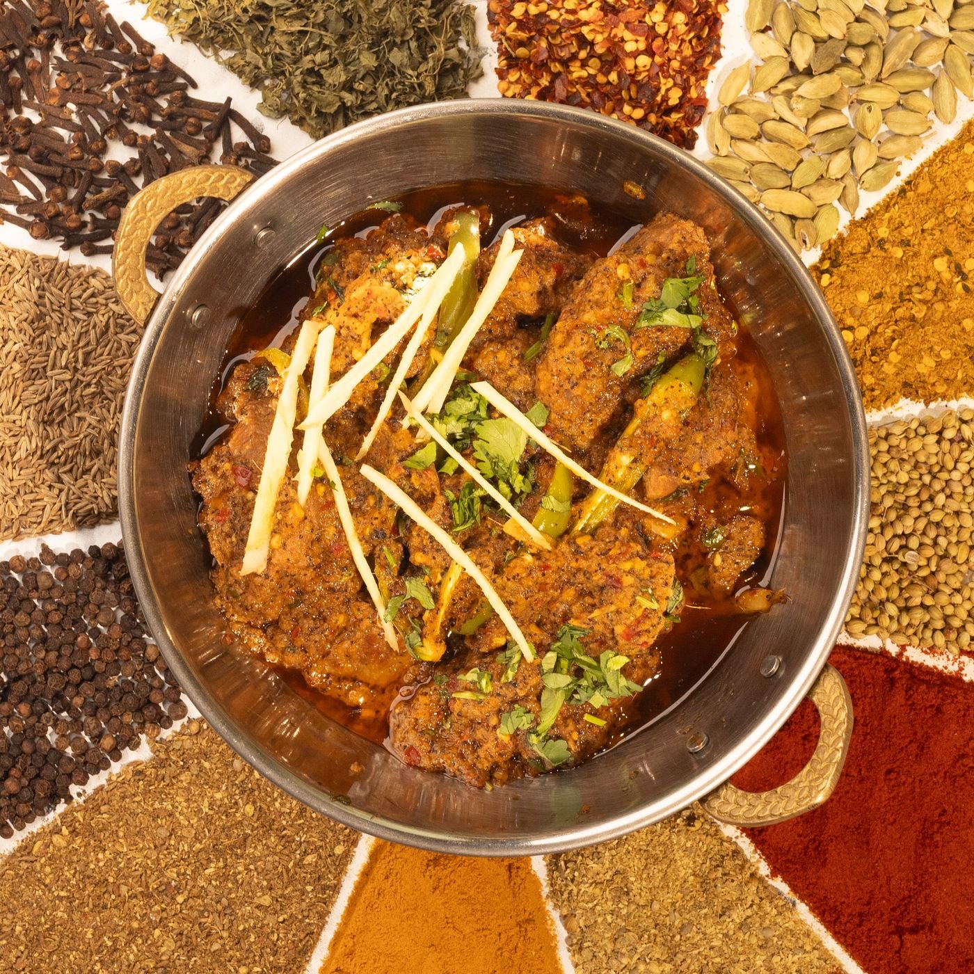Whole and ground spices arranged around a bowl of curry